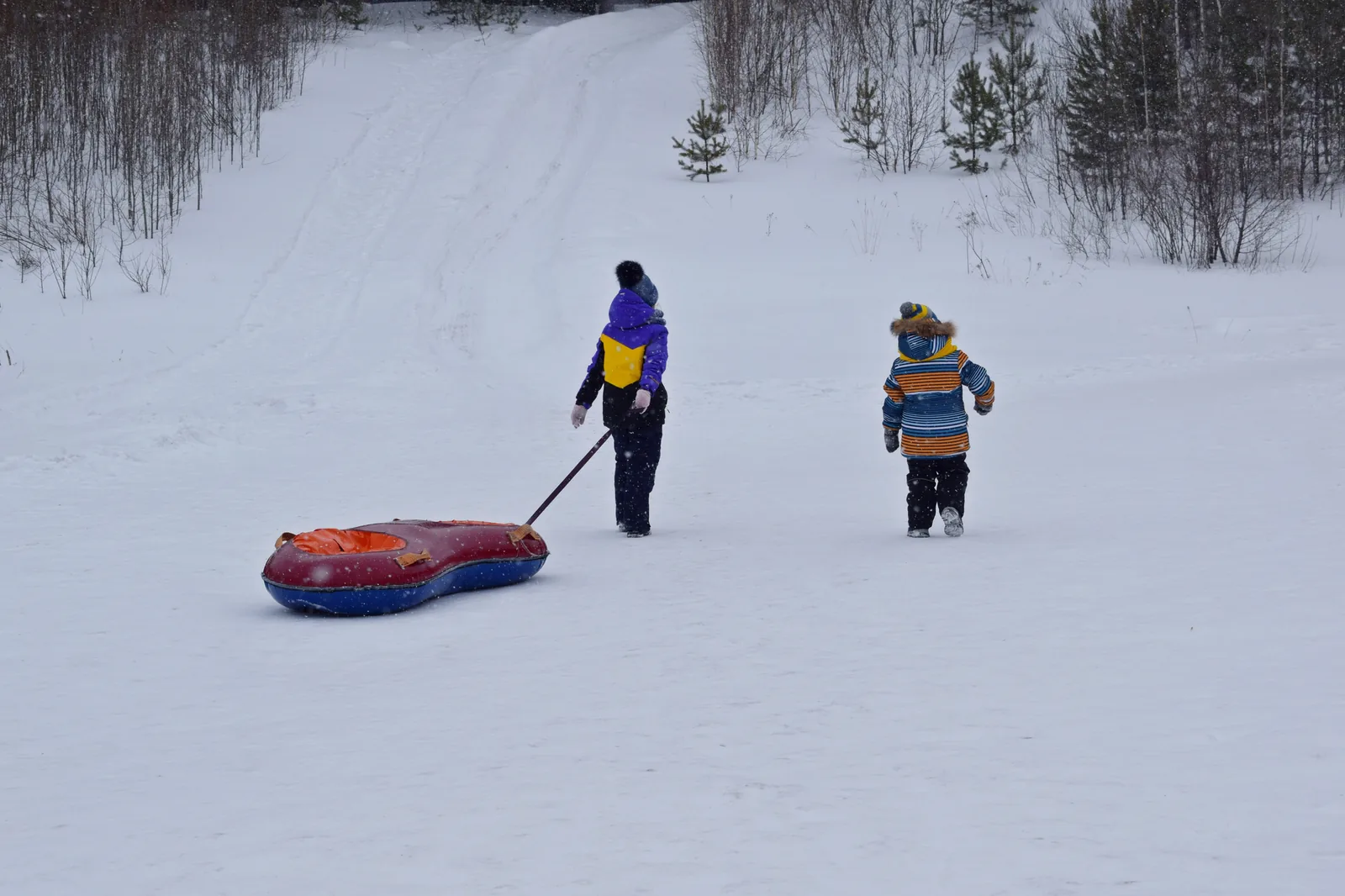 Two children pulling a snow tube across a snowy slope