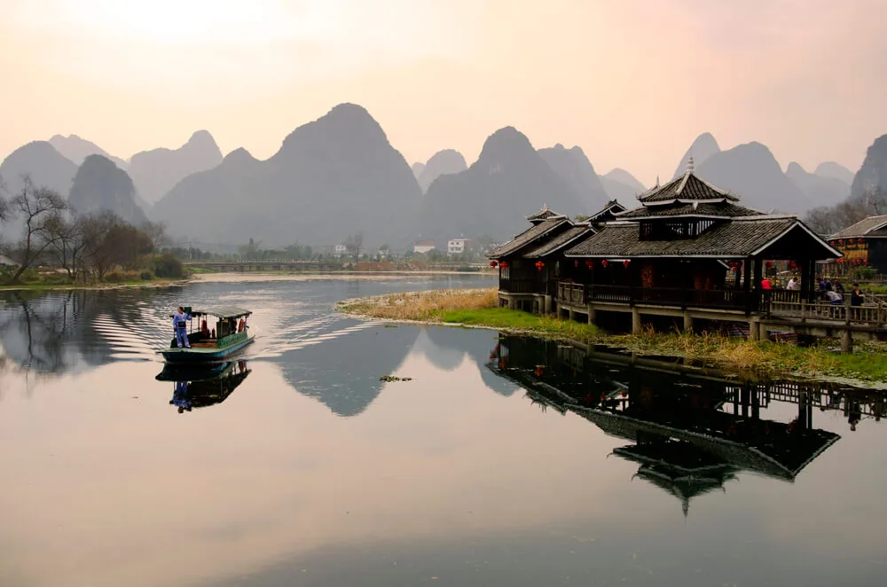 A boat crossing a still river below karst peaks near Yangshuo at dawn